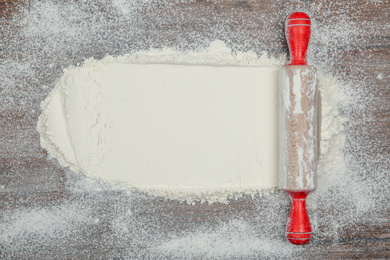Photo of Flour and rolling pin on wooden table, top view. Space for text