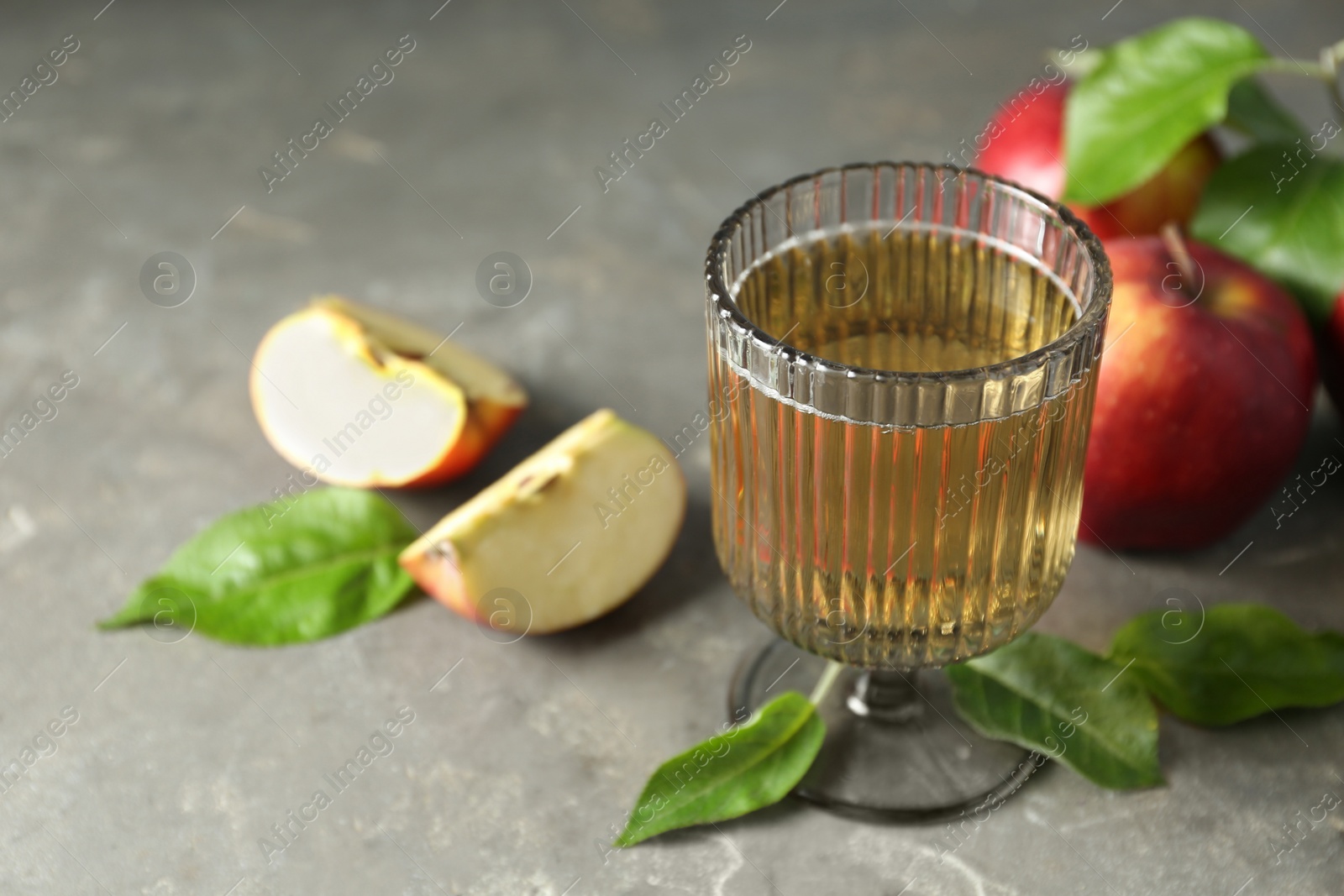 Photo of Glass of delicious cider, green leaves and apples on gray table, closeup. Space for text