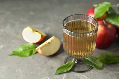 Photo of Glass of delicious cider, green leaves and apples on gray table, closeup. Space for text