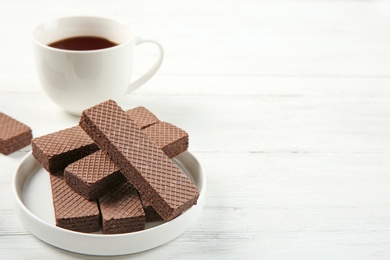 Photo of Plate of delicious chocolate wafers with cup of tea on white wooden background. Space for text