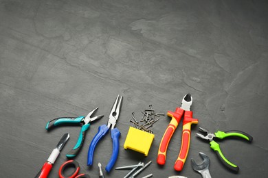 Different pliers, wrench, nails and other repair tools on black textured table, flat lay. Space for text