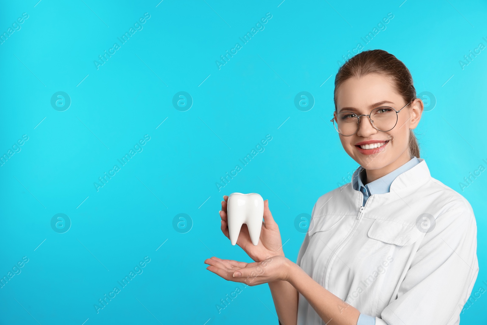 Photo of Female dentist holding tooth model on color background. Space for text