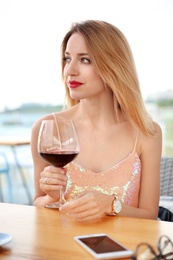 Photo of Young woman with glass of red wine at table outdoors