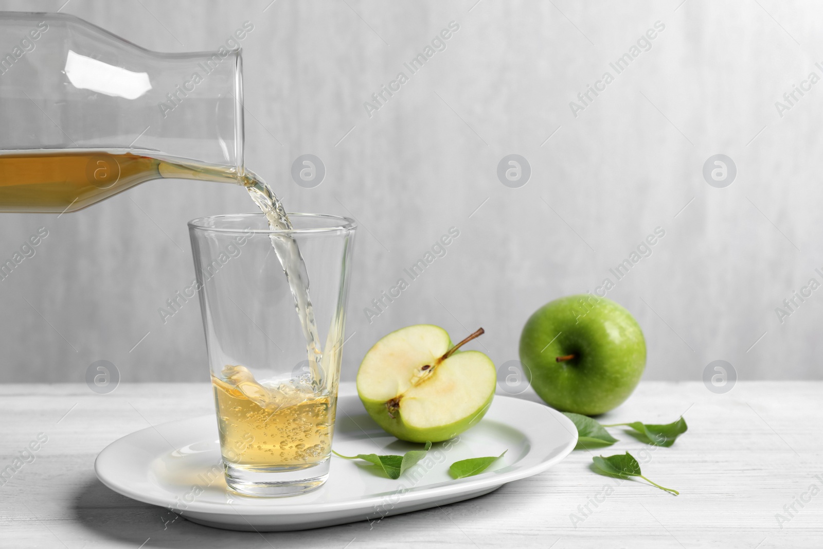 Photo of Pouring fresh apple juice into glass on white wooden table