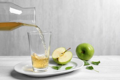 Photo of Pouring fresh apple juice into glass on white wooden table