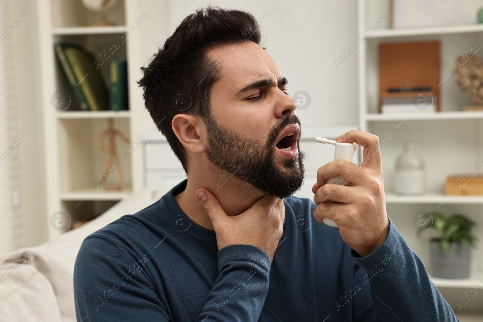 Photo of Young man using throat spray at home