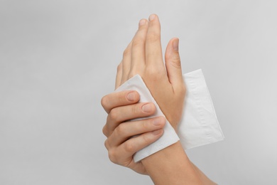 Photo of Woman cleaning hands with paper tissue on light background, closeup