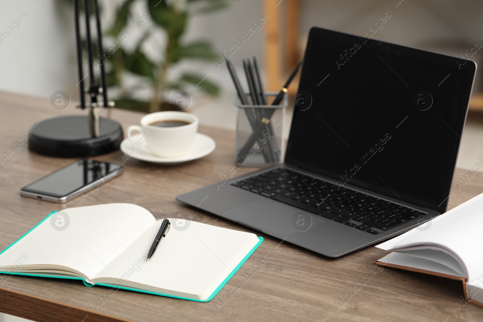 Photo of Home workspace. Modern laptop, notebook, cup of coffee and smartphone on desk in room