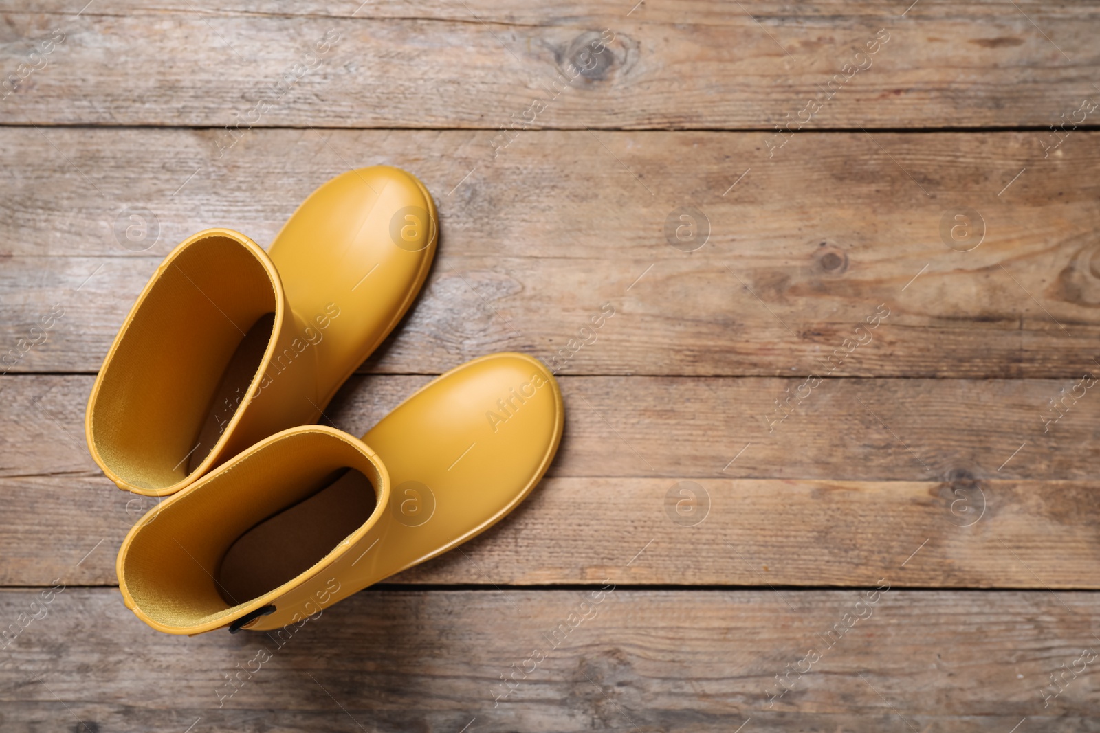 Photo of Yellow rubber boots on wooden background, top view. Space for text