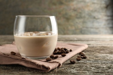 Coffee cream liqueur in glass and beans on wooden table, closeup