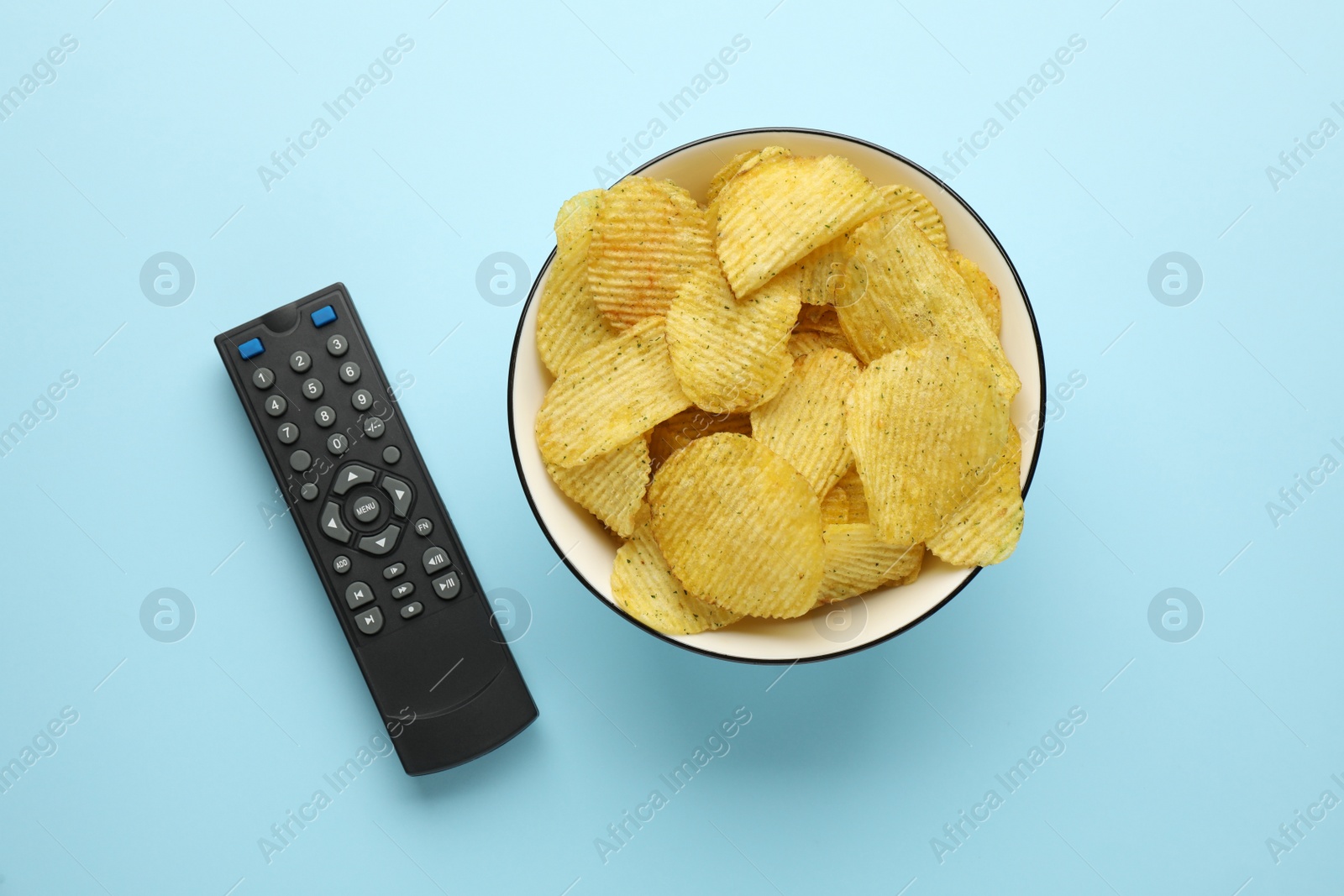 Photo of Remote control and bowl of potato chips on light blue background, flat lay