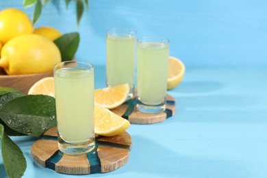 Photo of Tasty limoncello liqueur, lemons and green leaves on light blue table, space for text