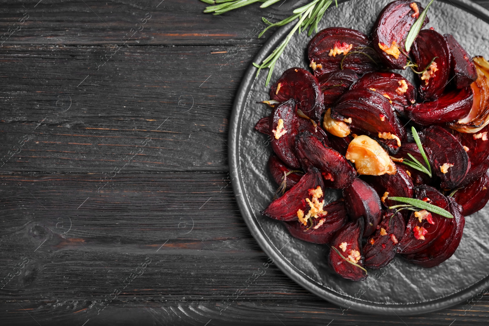 Photo of Roasted beetroot slices, garlic and rosemary on black wooden table, top view. Space for text