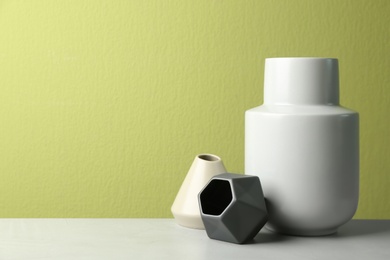 Photo of Stylish ceramic vases on grey stone table against green background. Space for text