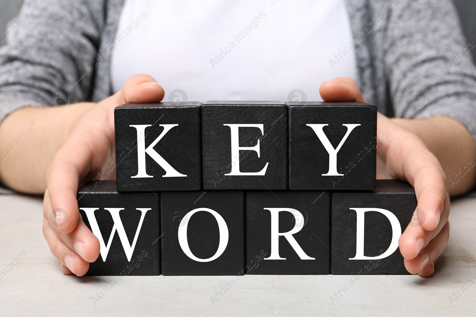 Photo of Woman demonstrating black cubes with word KEYWORD at light table, closeup