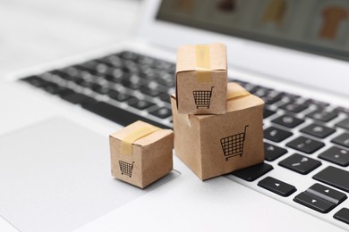 Image of Internet store. Small cardboard boxes with shopping carts on laptop, closeup