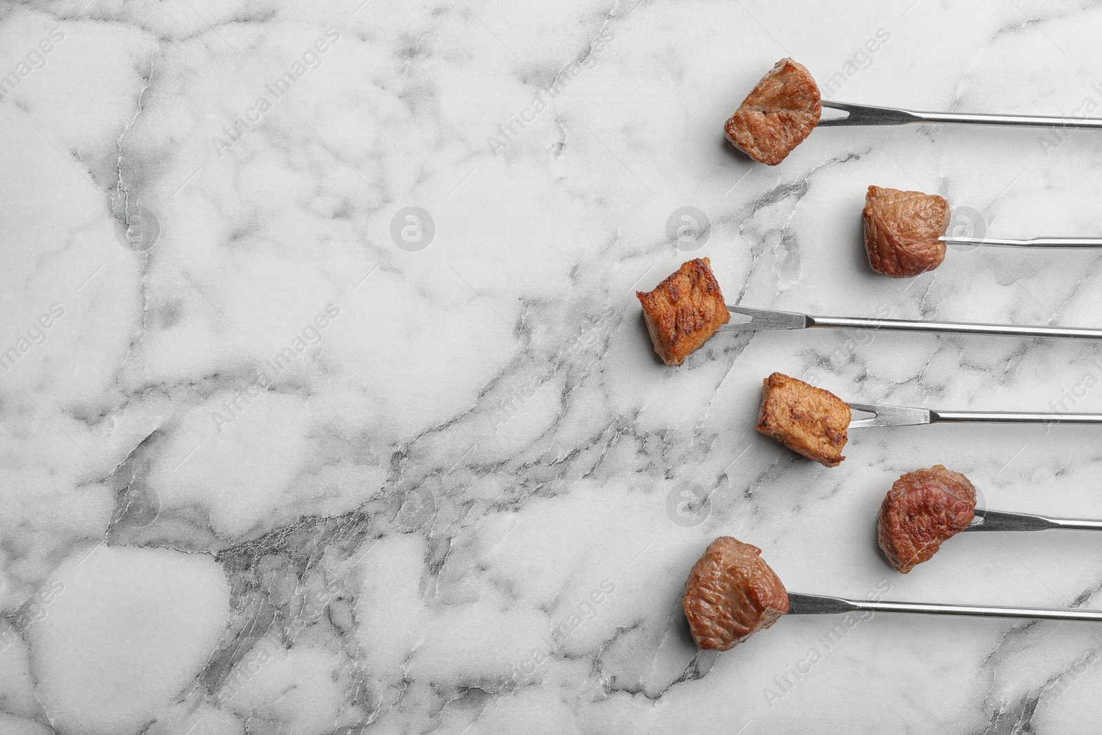 Photo of Forks with fried meat fondue pieces on marble background, top view. Space for text