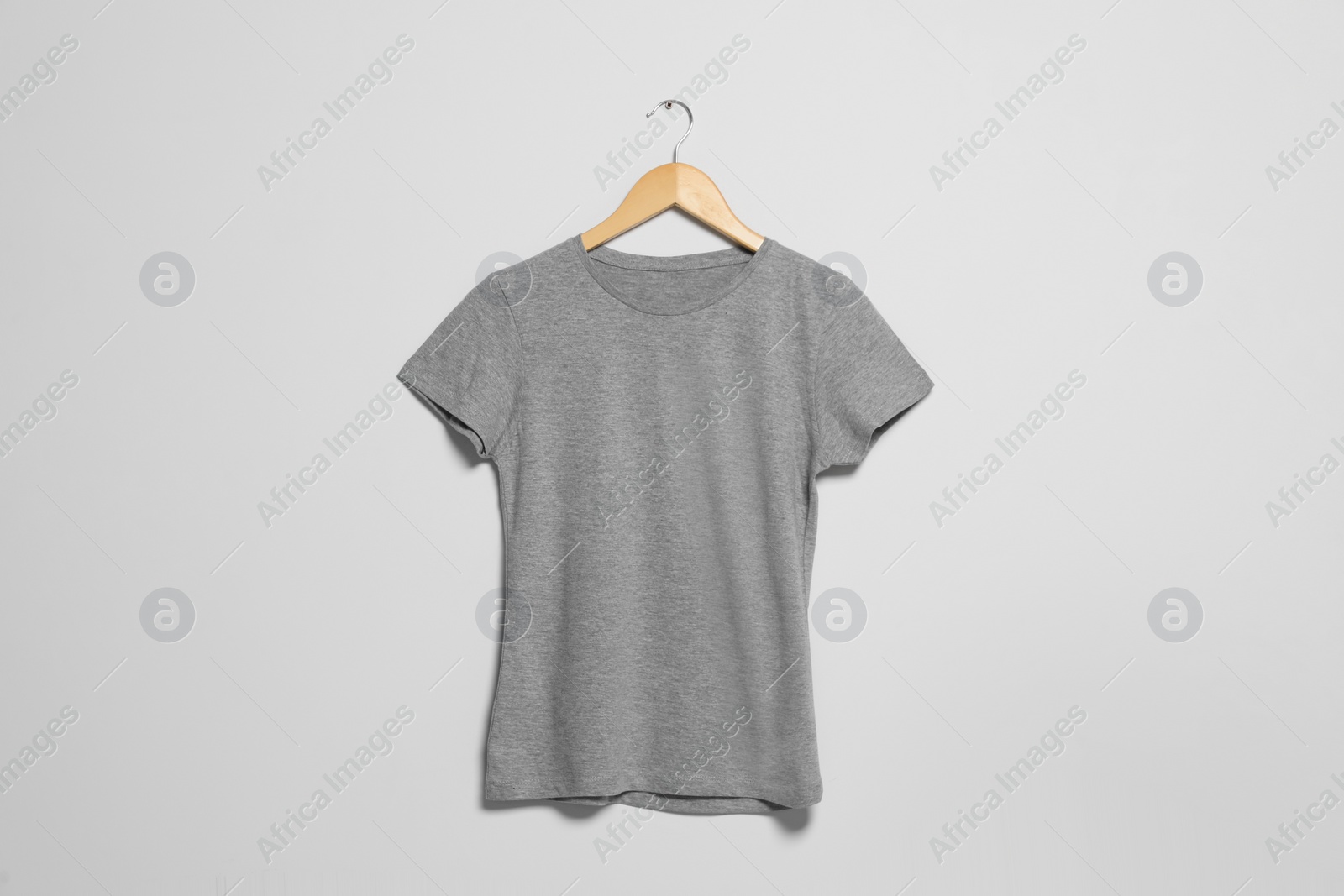 Photo of Hanger with grey t-shirt on light wall. Mockup for design