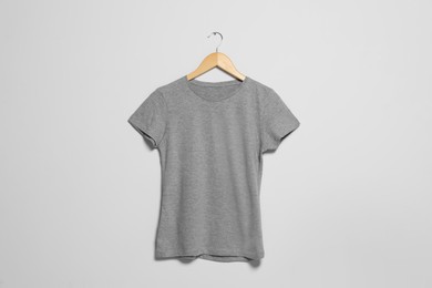 Hanger with grey t-shirt on light wall. Mockup for design