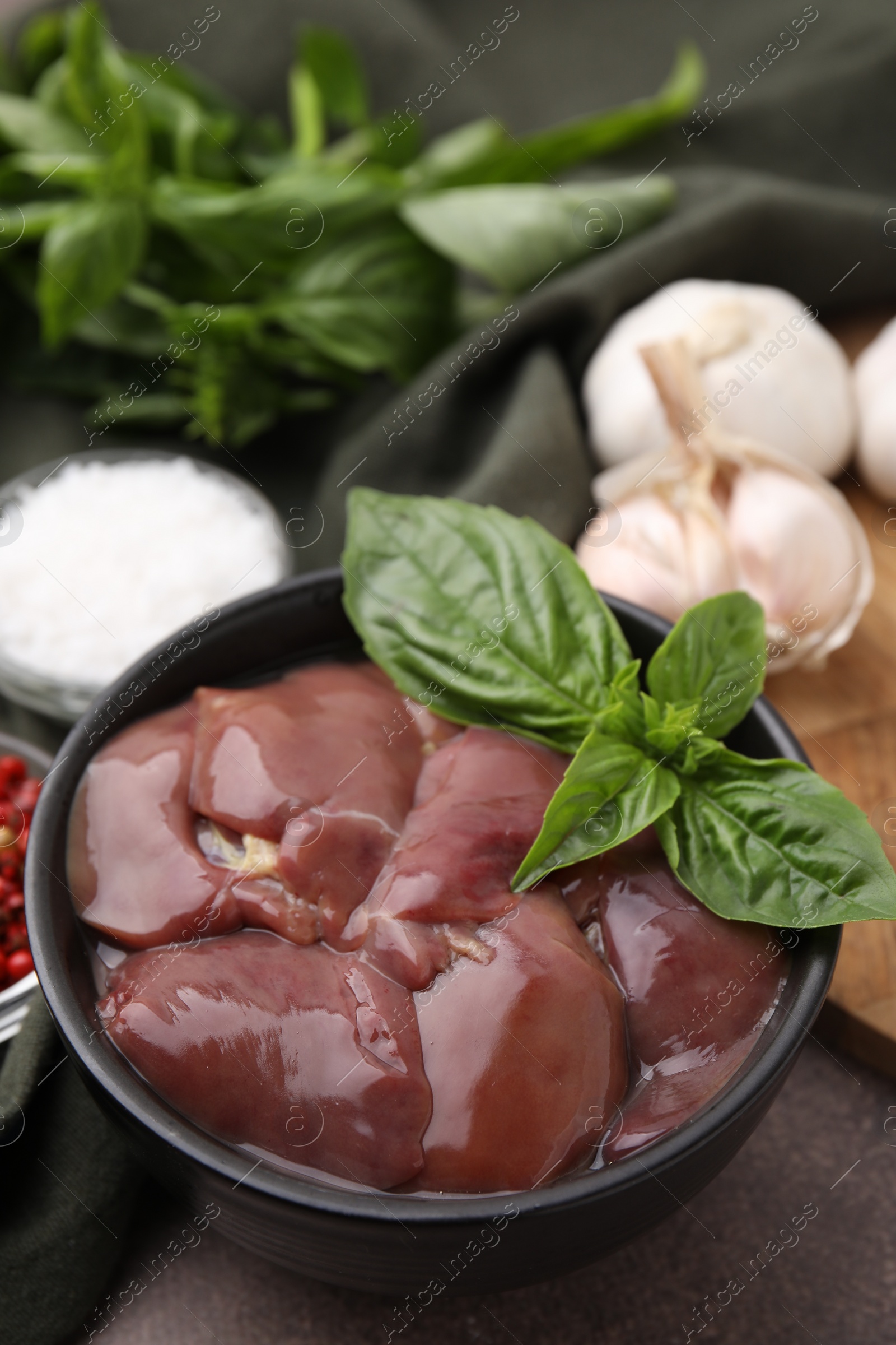 Photo of Bowl of raw chicken liver with basil on grey table, closeup