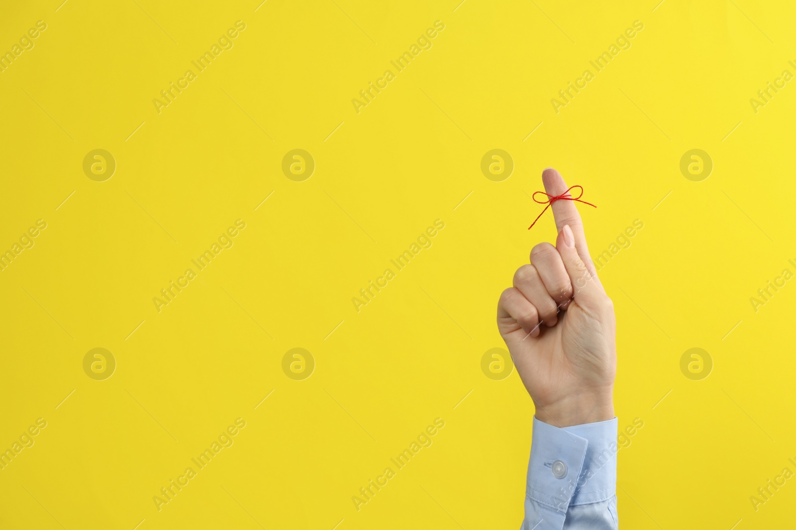 Photo of Woman showing index finger with tied red bow as reminder on yellow background, closeup. Space for text