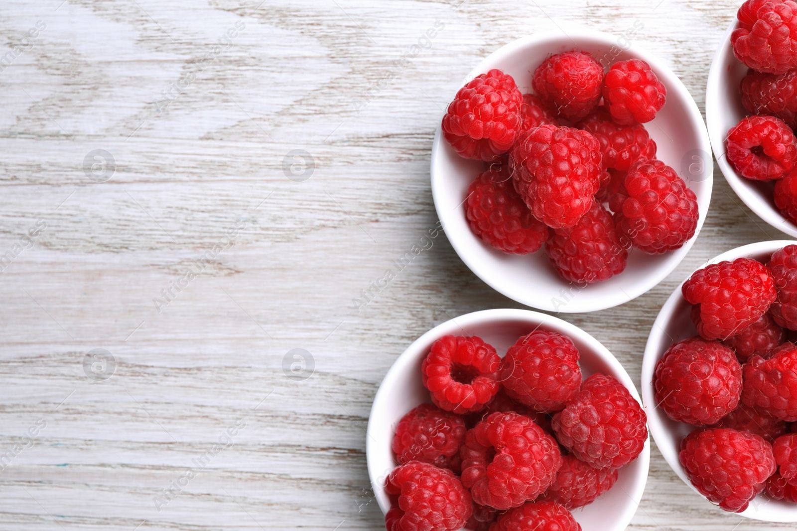 Photo of Tasty ripe raspberries on white wooden table, flat lay. Space for text