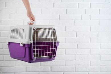 Photo of Woman holding violet pet carrier near white brick wall, closeup. Space for text
