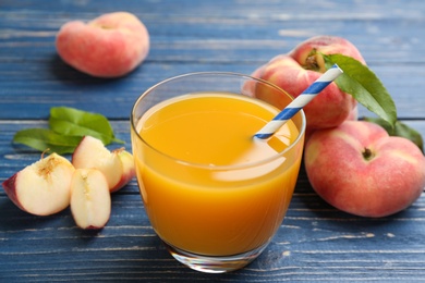 Photo of Natural peach juice and fresh fruits on blue wooden table, closeup
