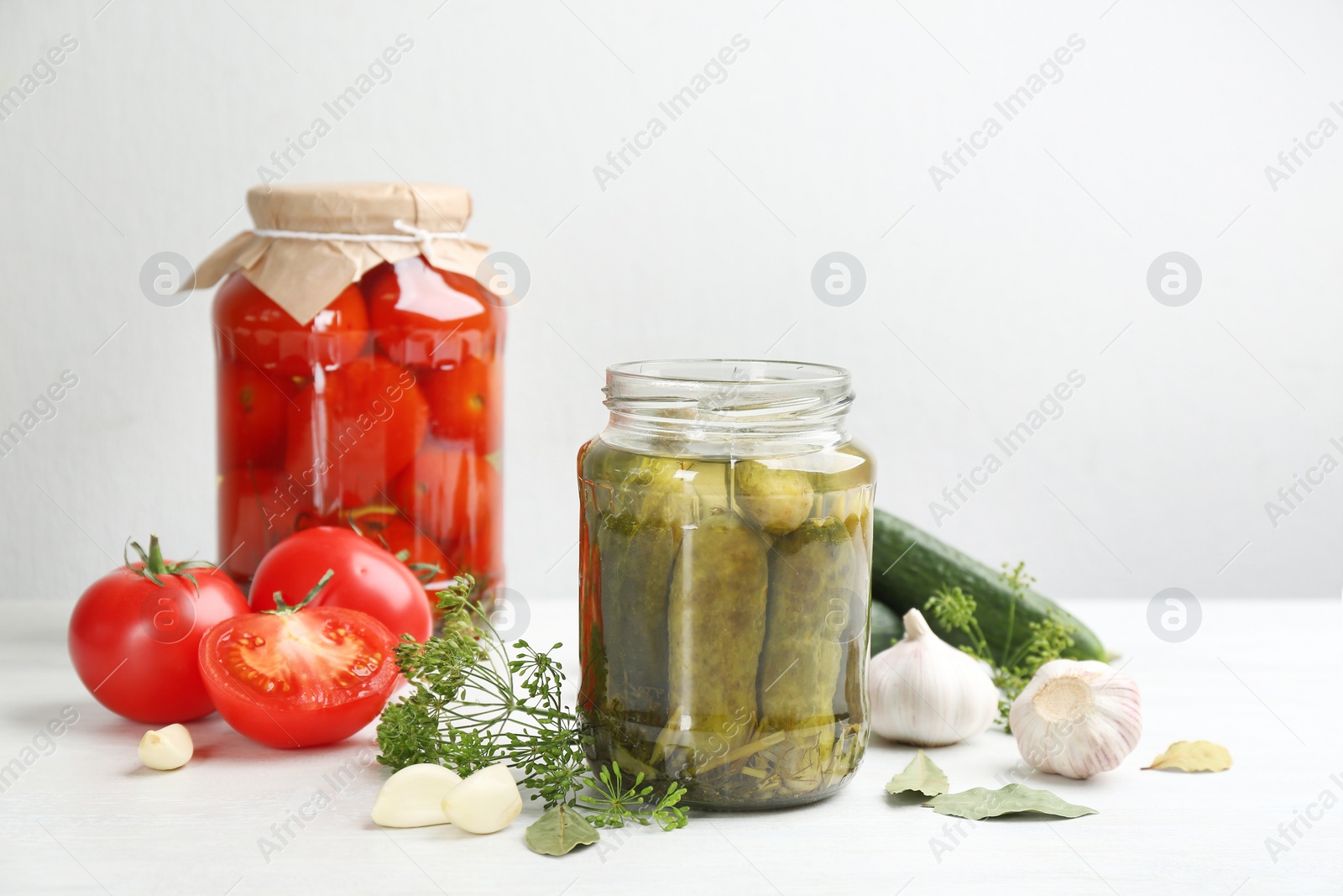 Photo of Glass jars of pickled cucumbers and tomatoes on white table