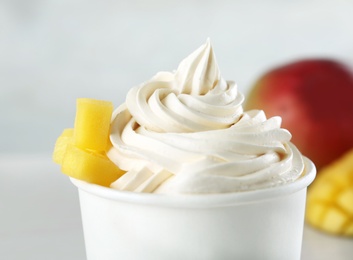 Photo of Cup with tasty frozen yogurt with mango on light background, closeup