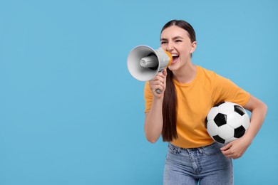 Photo of Soccer fan with ball shouting in megaphone on light blue background. Space for text