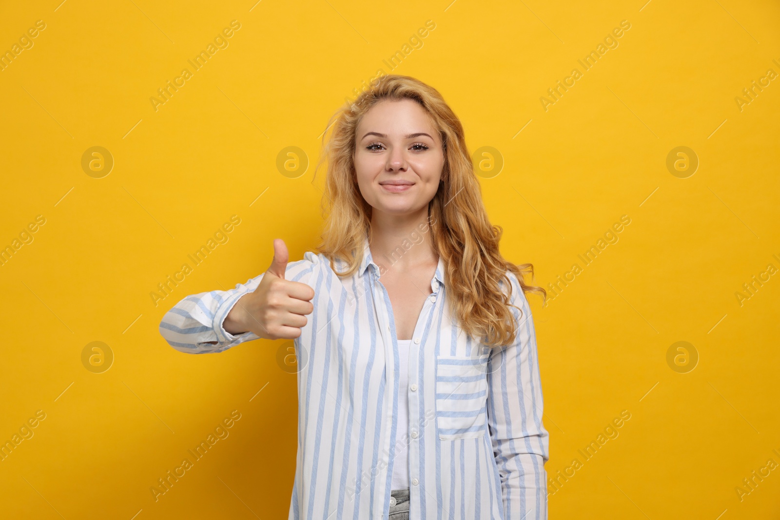 Photo of Happy young woman showing thumb up gesture on yellow background