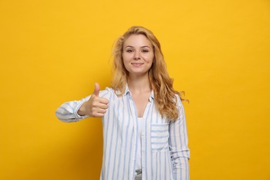 Happy young woman showing thumb up gesture on yellow background