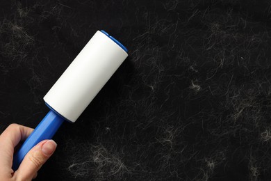 Photo of Woman with lint roller removing pet hair from black fabric, top view. Space for text