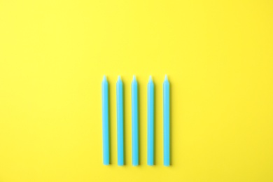 Photo of Blue birthday candles on yellow background, top view