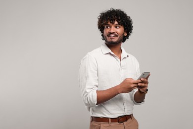 Handsome smiling man using smartphone on light grey background, space for text