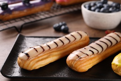 Plate with tasty glazed eclairs on table, closeup