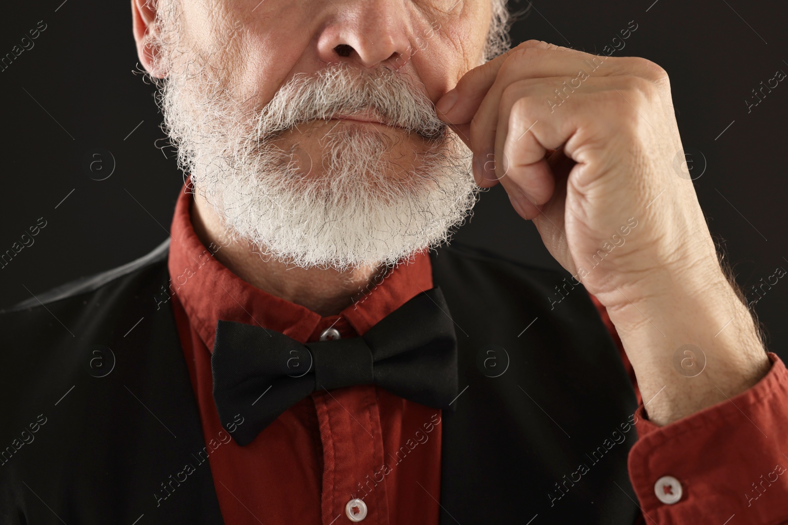 Photo of Man touching mustache on black background, closeup