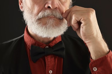 Man touching mustache on black background, closeup