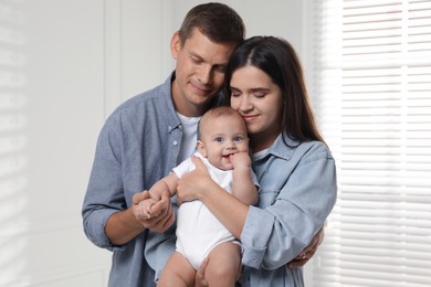 Photo of Happy family. Couple with their cute baby near window indoors