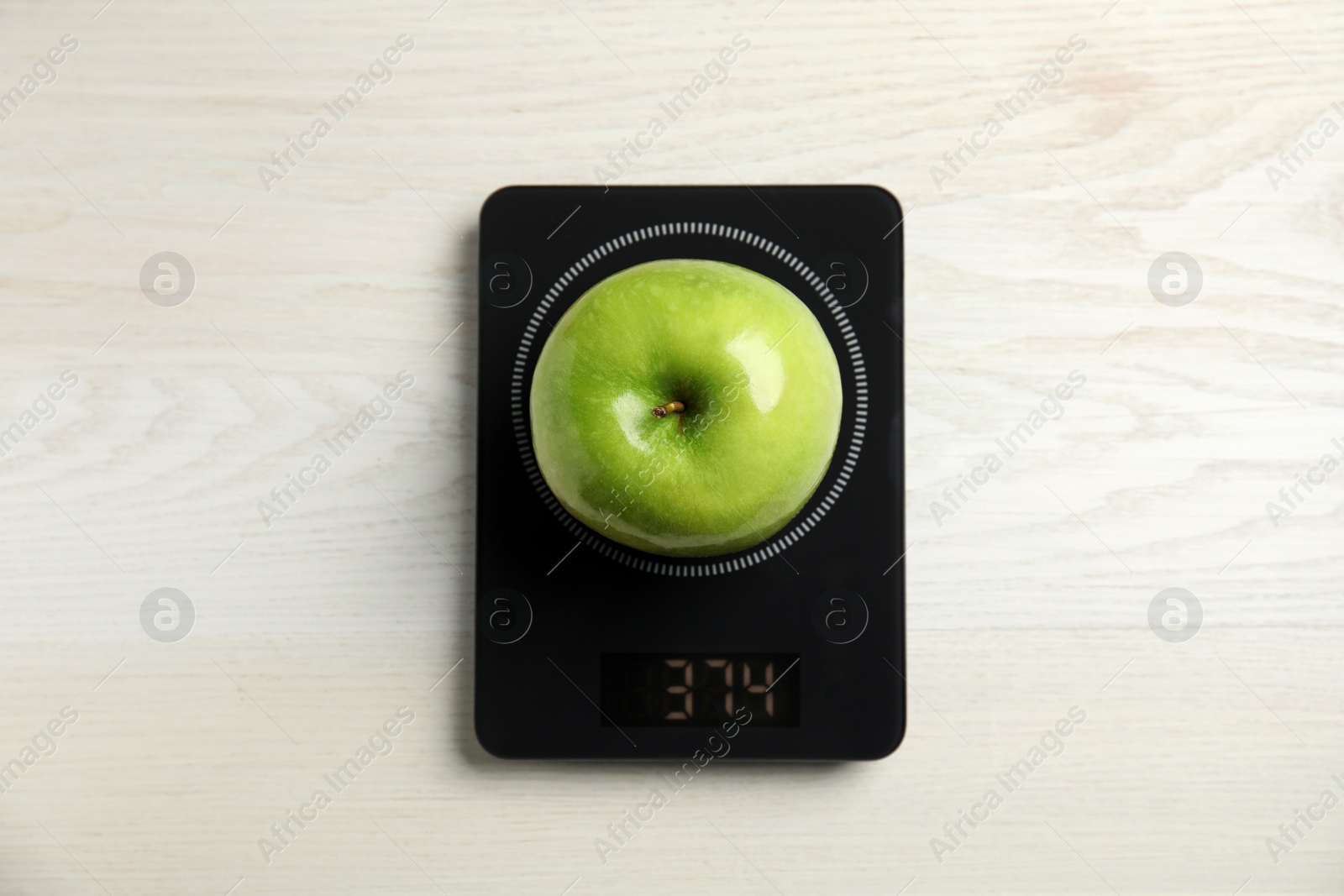Photo of Ripe green apple and electronic scales on white wooden table, top view