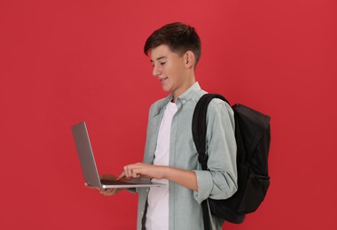 Teenage student with backpack and laptop on red background