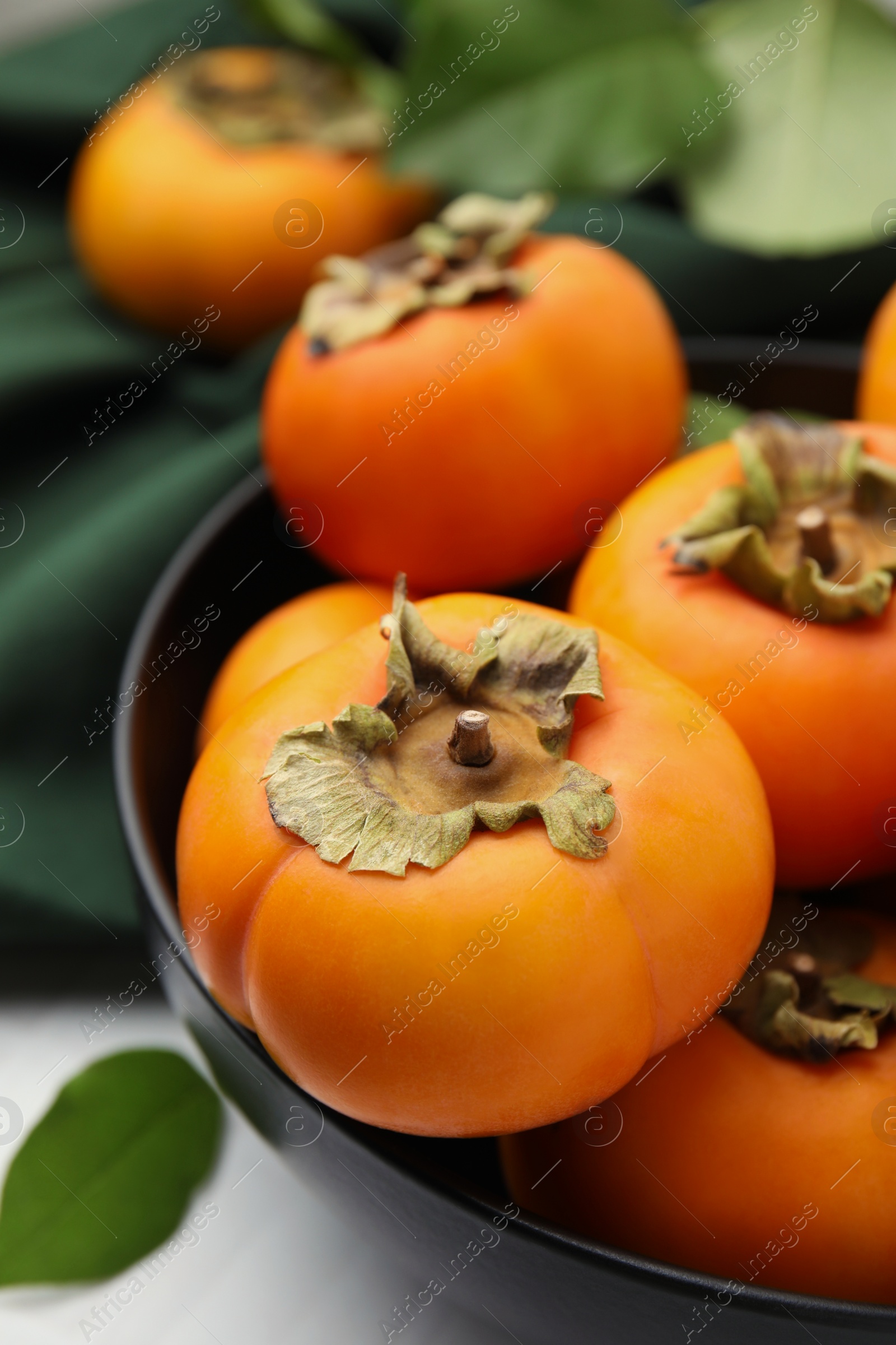 Photo of Bowl with delicious ripe juicy persimmons on white table, closeup