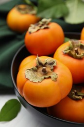 Bowl with delicious ripe juicy persimmons on white table, closeup