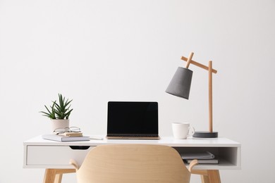 Photo of Workplace with laptop, office stationery on desk and chair near white wall