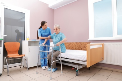 Nurse assisting senior woman with walker to get up from bed in hospital ward