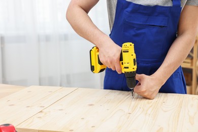 Young worker using electric drill at table in workshop, closeup