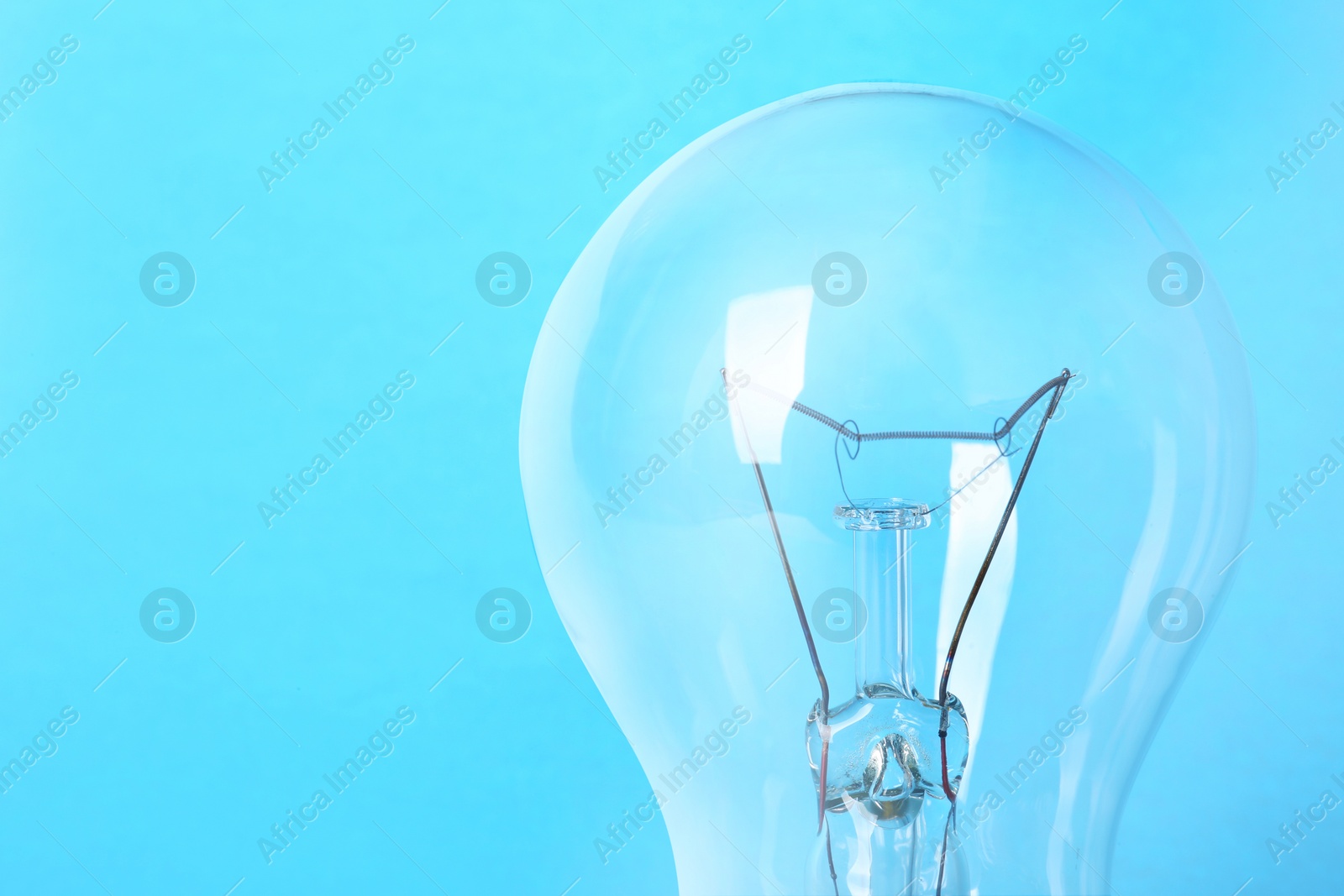 Photo of New modern lamp bulb on light blue background, closeup. Space for text