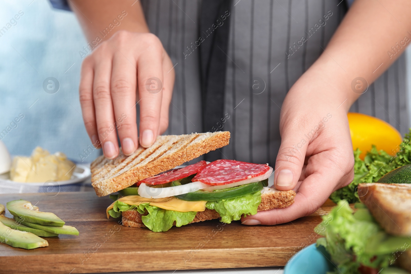 Photo of Woman making tasty sandwich with sausage at  table, closeup