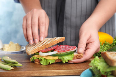 Photo of Woman making tasty sandwich with sausage at  table, closeup